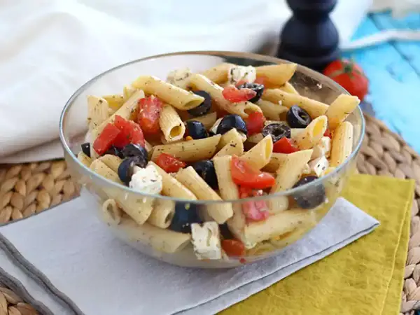 En härlig italiensk pastasallad med penne, tomater, svarta oliver och fetaost i en glasskål. Perfekt för en lätt lunch.
