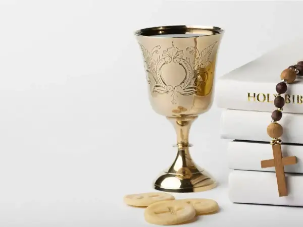 Złoty kielich, hostie, różaniec i stos białych ksiąg, w tym "Holy Bible". Symbolika sakramentu, jak akt chrztu.