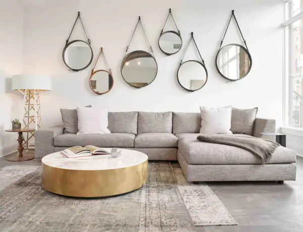 En soffgrupp med grå soffa, marmorbord och flera runda speglar på väggen skapar en elegant art deco inredning.