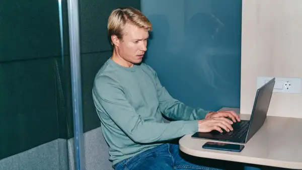 Man i ljudisolerad bås jobbar intensivt på laptop, kanske funderar på konsekvenserna av illojalitet mot arbetsgivare och skadestånd.