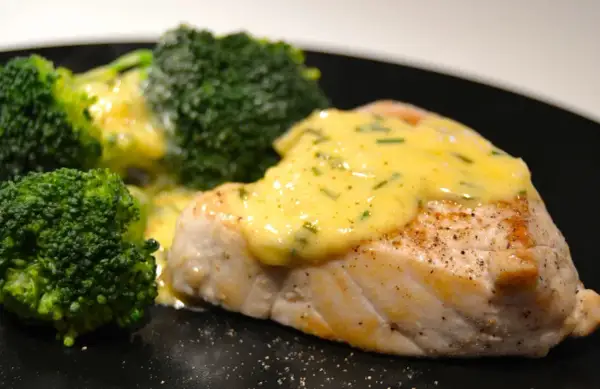 En saftig fiskfilé med krämig sås till tonfisk och gröna broccolibuketter på en svart tallrik.