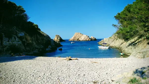 La cala Ferriol, con su playa de guijarros y aguas cristalinas, invita a disfrutar del sol y el mar. Barcas y bañistas comparten este paraíso.