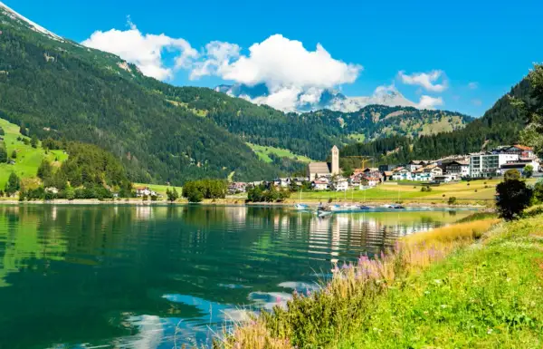 Incantevole lago alpino con barche a vela, circondato da verdi montagne e pittoreschi borghi Trentino Alto Adige.