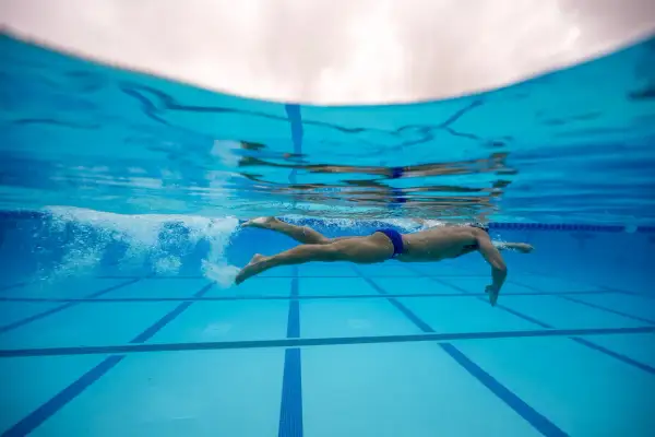 Underwater view of a swimmer performing flutter kicks, propelling through the blue pool water.