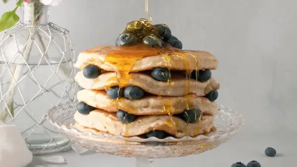Pancake senza latte, una torre dorata con mirtilli freschi e sciroppo d'acero che cola.