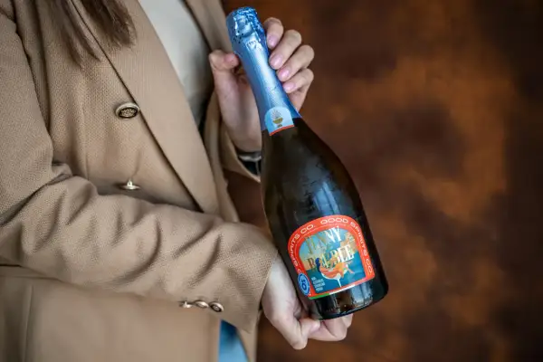 Kobieta w beżowym żakiecie trzyma butelkę musującego napoju, idealnego na międzynarodowy dzień prosecco.