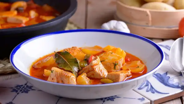 Un plato humeante de patatas con bonito, con trozos de pescado tierno y patatas en una salsa roja sabrosa, adornado con hojas de laurel.
