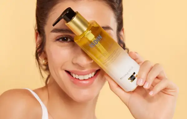 Mujer sonriente sostiene una botella de aceite de ducha ISDIN.