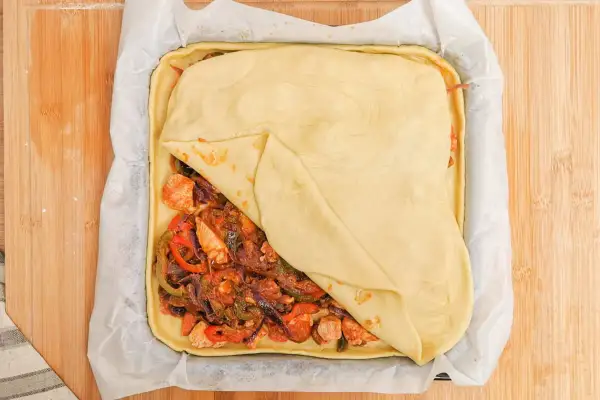 Empanada de pollo lista para hornear, con relleno de pollo y verduras cubierto por masa dorada.