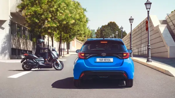 Niebieski Toyota Yaris HEV. Kierowca na skuterze obok. Szukasz "toyota yaris instrukcja obsługi po polsku"?