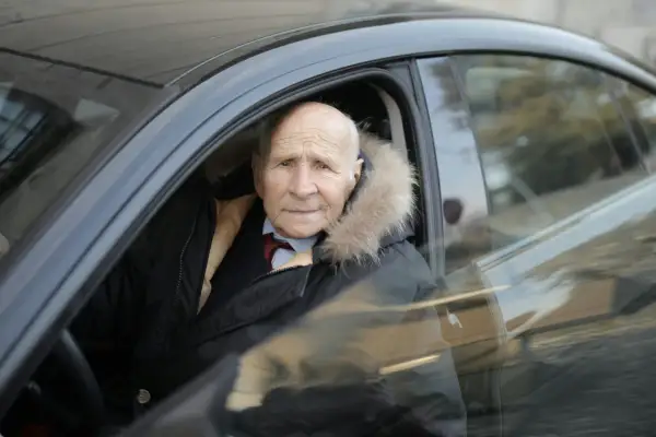 Un homme âgé, au regard vif, est assis au volant de sa voiture, prêt à prendre la route. Son permis de conduire senior lui permet de garder son indépendance.