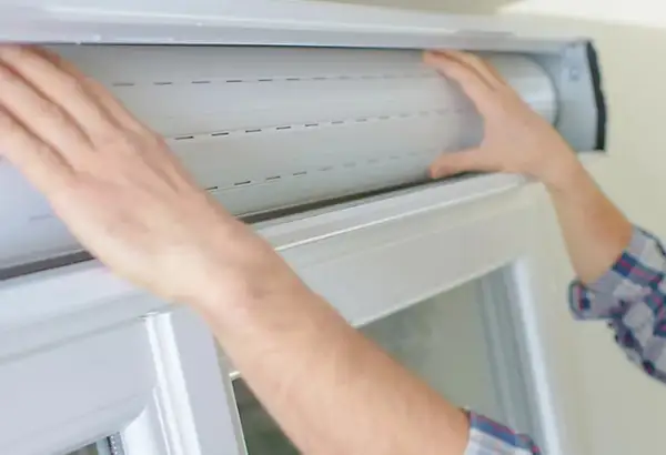 Mains manipulant un volet roulant blanc, étape clé pour savoir comment réparer un volet roulant.