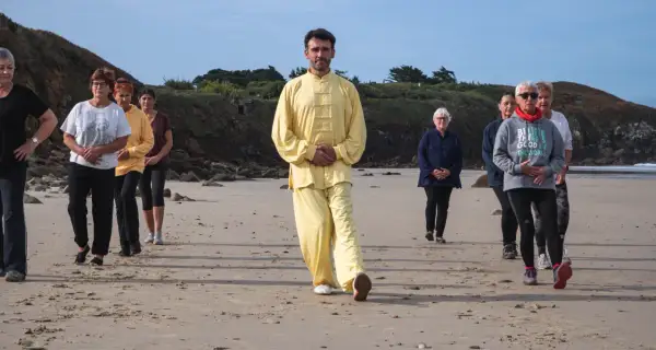 Un groupe suit un homme en tenue jaune lors d'une marche afghane sur une plage.