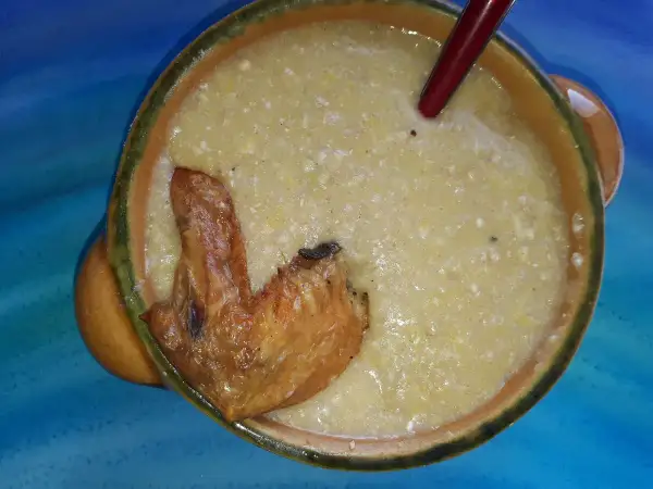 Herzhafte polenta taragna mit einem knusprigen Hähnchenflügel in einer rustikalen Schüssel.