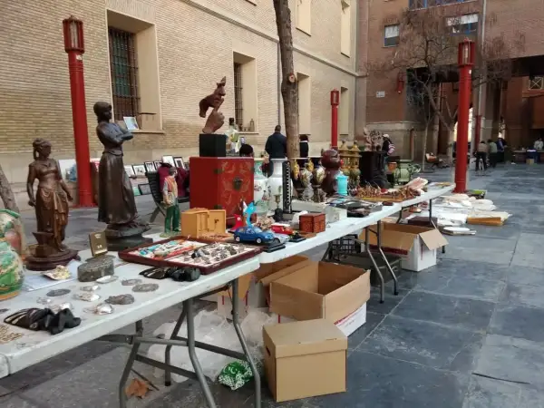 Mercado de antigüedades en Zaragoza con estatuas, jarrones y objetos curiosos en mesas al aire libre.