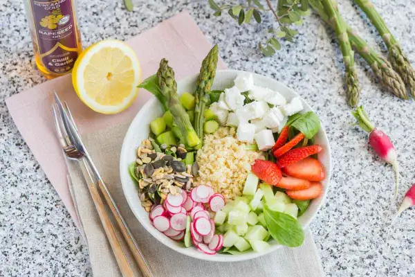 Un plat végétarien coloré avec du quinoa, des asperges, des fraises, du concombre, des radis, des graines et du fromage feta.