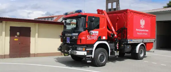 Czerwony strażak OSP Scania z żurawiem i plandeką z godłem Polski gotowy do akcji.
