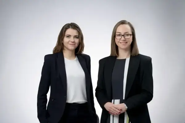 Dwie kobiety w garniturach, prawniczki, na jasnym tle.