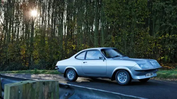 Silver Vauxhall Firenza på en väg kantad av träd. Solen skiner genom grenarna.