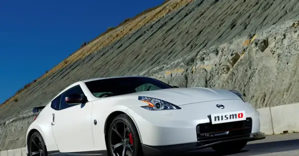 Biały Nissan 370Z Nismo z czerwonymi akcentami na lusterkach i zaciskach hamulcowych, zaparkowany na tle skalistego zbocza.