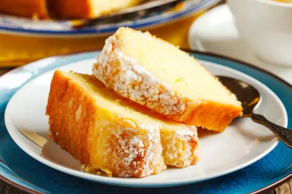 Deux parts de gâteau au yaourt moelleux, saupoudrées de sucre glace, sur une assiette blanche avec une cuillère ornée.