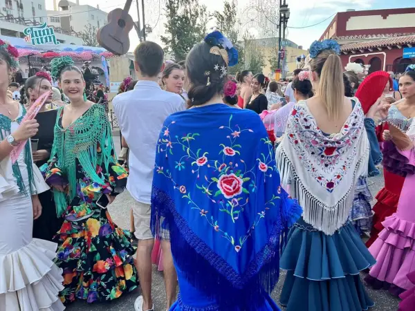 Mujeres con trajes de flamenca y mantones bordados, uno azul con flores rojas y otro blanco con detalles coloridos.