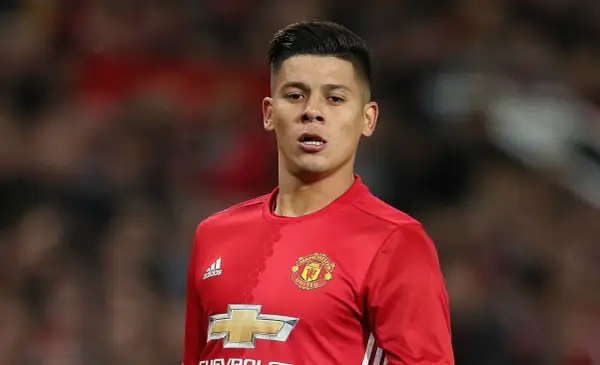 Piłkarz w czerwonej koszulce Manchester United, z logo klubu i Adidasa. Rojo wiek, skupiony na boisku.