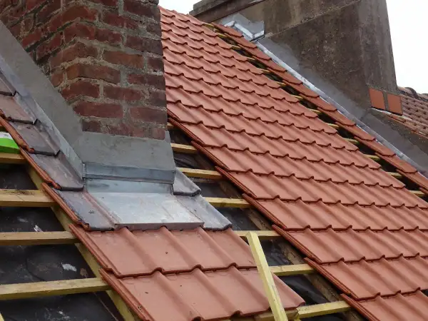 Dachdecker arbeiten am Schornstein, um ihn abzudichten. Neue rote Dachziegel werden verlegt.