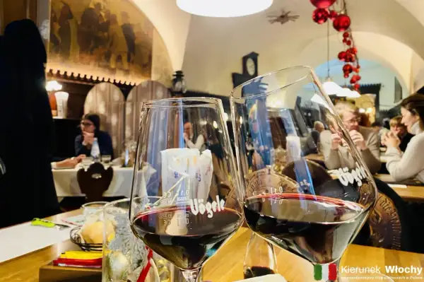 Dwa kieliszki pełne ciemnoczerwonego lagrein wino, w tle restauracja z ludźmi i świątecznymi ozdobami.