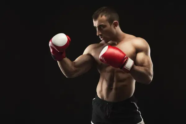 Muscular boxer in red gloves and black shorts in a defensive stance against a black background.