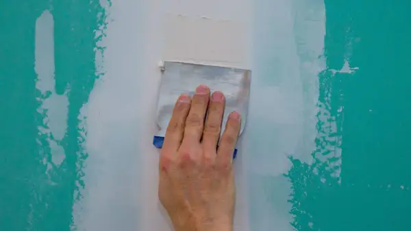 Main d'un artisan ponçant un mur à la main avec une spatule pour lisser le plâtre.