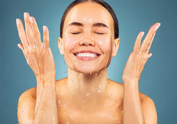 Donna sorridente con acqua sul viso e mani. L'acqua micellare a cosa serve? A detergere e rinfrescare la pelle.