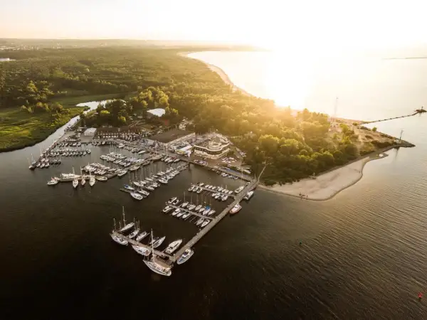 Zachód słońca nad zatoką, gdzie cumują liczne jachty. Widok na górki zachodnie marina, otoczoną zielenią i piaszczystą plażą.