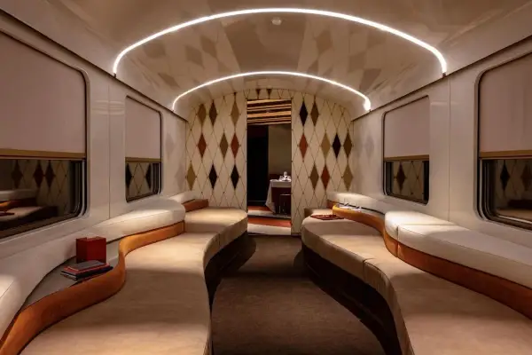 Luxuriöses Interieur eines Nachtzugs nach Italien mit geschwungenen Sofas, Rautenmuster-Tapete und indirekter Beleuchtung.