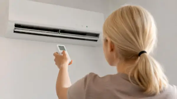 Donna bionda con telecomando davanti a un condizionatore. Guida su come scegliere condizionatore.