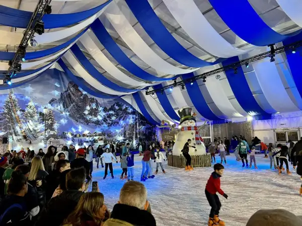 Pista de hielo en Zaragoza, Plaza del Pilar, con un gran muñeco de nieve y gente patinando bajo un techo de telas azules y blancas.