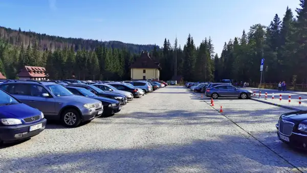Duży parking przy Palenicy Białczańskiej, pełen samochodów, z górami i lasem w tle.