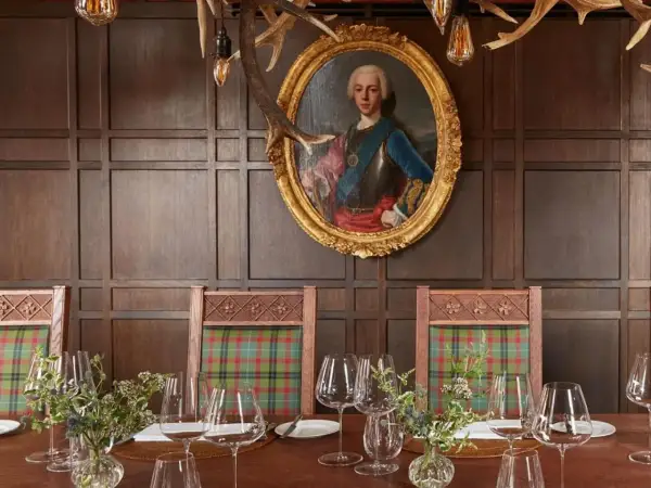 Un ritratto regale domina la sala da pranzo, con sedie a quadri e un tavolo apparecchiato, un'ambientazione che evoca i migliori ristoranti di Londra.
