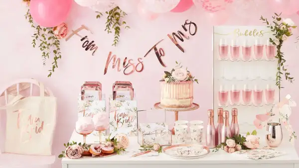 Uroczy stół na wieczór panieński: tort, babeczki, balony, girlanda "From Miss To Mrs" i kieliszki z różowym napojem.