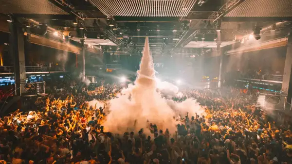 Folla in delirio in una **fabrik discoteca** con un getto di fumo che sale verso il soffitto.
