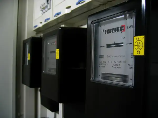 Trzy liczniki energii elektrycznej, każdy pokazujący inną jednostkę energii. Jeden z nich wskazuje 3104572 kWh.