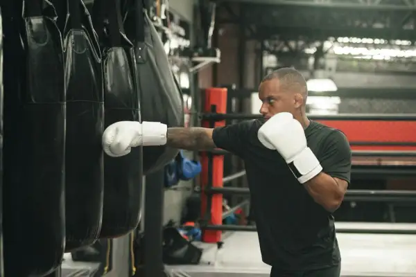 Man in white boxing gloves throws a punch at a heavy bag, demonstrating how to practice boxing without a bag.