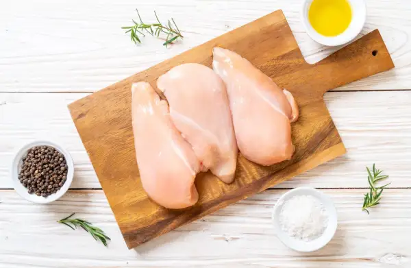 Tre petti di pollo crudi su tagliere, con pepe nero, sale, rosmarino e olio. Ideale per un pasto leggero, con poche calorie petto di pollo.