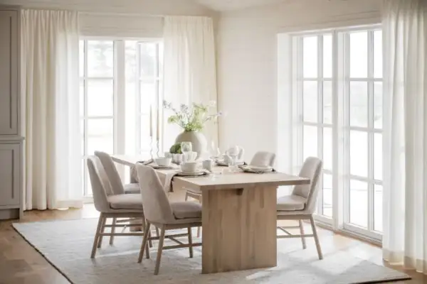 Ljus och luftig matplats med inspiration från naturen. Träbord, beiga stolar och stora fönster med vita gardiner skapar en harmonisk känsla.