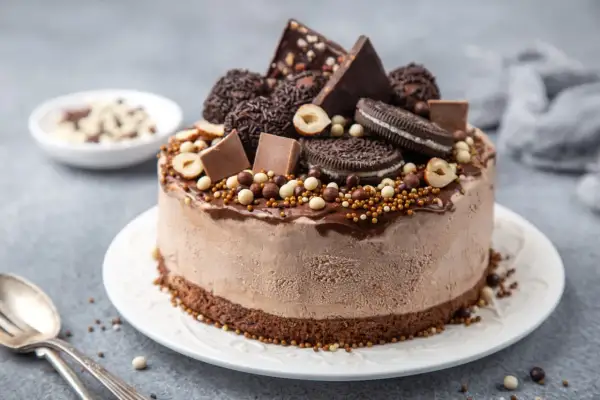 En chokladglassbakelse dekorerad med chokladbitar, oreos, hasselnötter och strössel. Enkel chokladsås rinner ner längs sidorna.