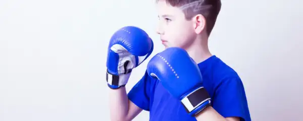 Young boxer in a wide boxing stance, wearing blue gloves and shirt, ready to fight.