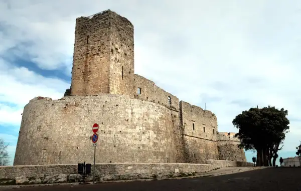 Imponente castello di Monte Sant'Angelo, con mura in pietra grezza e un torrione svettante sotto un cielo nuvoloso.
