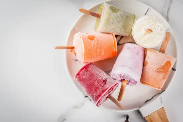 Variopinti ghiaccioli fatti in casa su un piatto bianco: rossi, arancioni, rosa, verdi e bianchi al cocco.