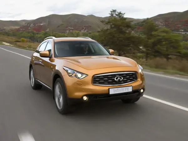 Pomarańczowy Infiniti QX70 jedzie po drodze wśród jesiennych wzgórz.