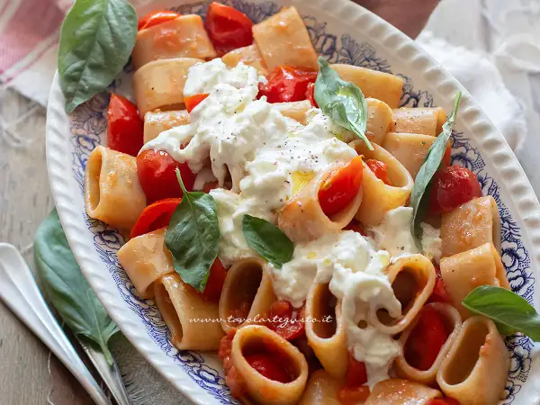 Piatto di pasta paccheri con pomodorini freschi e burrata cremosa, guarnito con basilico.